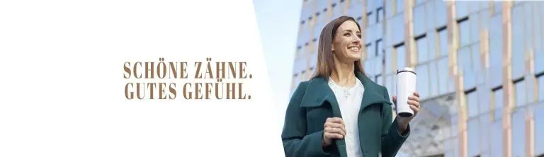 Eine lächelnde Frau in einem grünen Mantel steht im Freien in der Nähe eines modernen Glasgebäudes und hält einen weißen Reisebecher in der Hand. Links ist auf weißem Hintergrund der deutsche Text „SCHÖNE ZÄHNE. GUTES GEFÜHL.“ zu sehen, der auf dezente Weise das Selbstbewusstsein widerspiegelt, das die Ästhetische Zahnheilkunde Kronberg vermittelt.